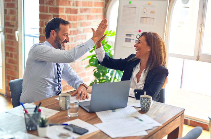Two colleagues celebrating with a high five at their desk